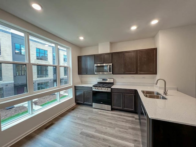 kitchen featuring appliances with stainless steel finishes, light wood-type flooring, dark brown cabinetry, light stone countertops, and sink