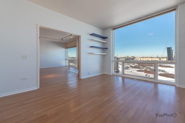 unfurnished room featuring rail lighting, floor to ceiling windows, baseboards, and wood finished floors