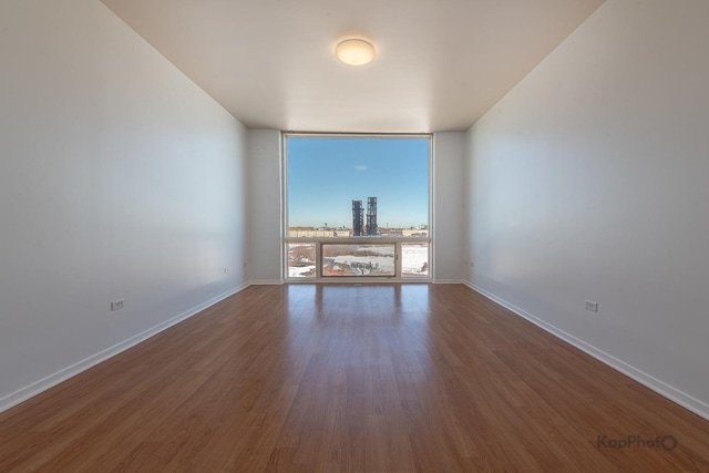 empty room featuring baseboards, a city view, dark wood-style floors, and floor to ceiling windows