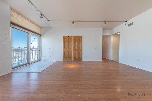 spare room with baseboards, light wood finished floors, visible vents, and track lighting