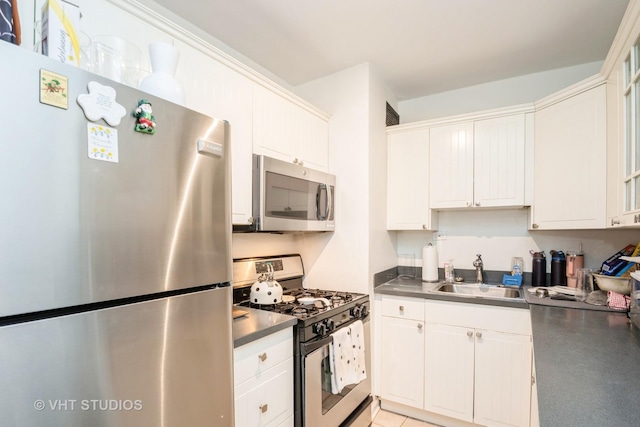 kitchen featuring dark countertops, appliances with stainless steel finishes, white cabinets, and a sink