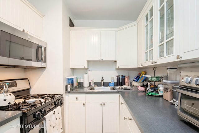 kitchen with gas range, dark countertops, glass insert cabinets, and white cabinetry