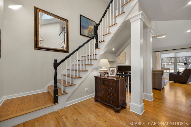 stairway with a high ceiling, wood finished floors, decorative columns, and baseboards