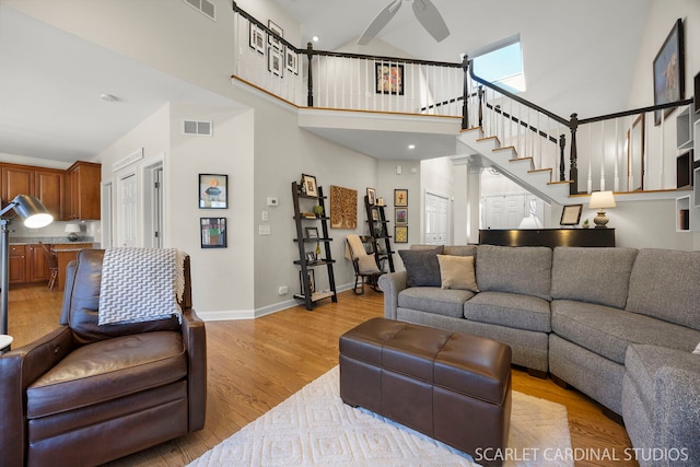 living area featuring visible vents, a towering ceiling, a ceiling fan, light wood-type flooring, and baseboards