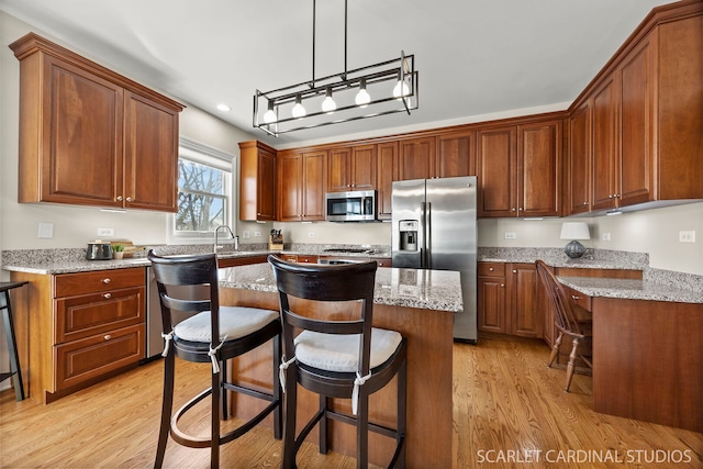 kitchen with light stone counters, a center island, appliances with stainless steel finishes, brown cabinets, and decorative light fixtures