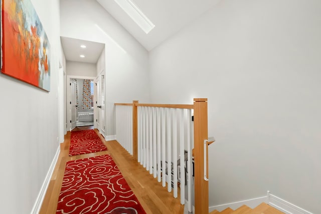 hall with a skylight, an upstairs landing, wood finished floors, high vaulted ceiling, and baseboards