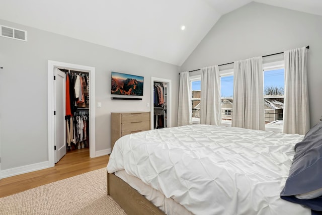 bedroom with lofted ceiling, visible vents, light wood-style flooring, a spacious closet, and baseboards