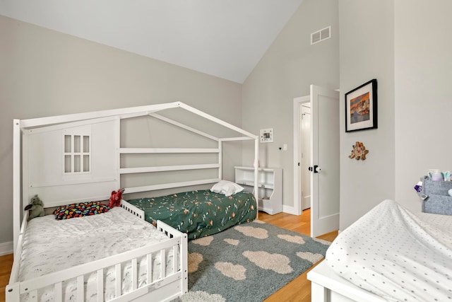 bedroom with high vaulted ceiling, visible vents, baseboards, and wood finished floors