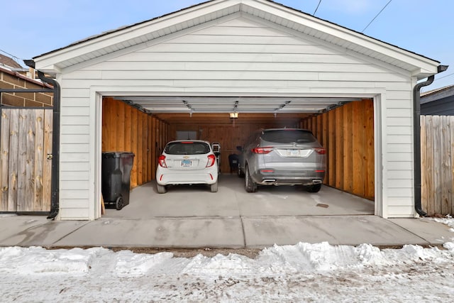 snow covered garage featuring a detached garage and fence