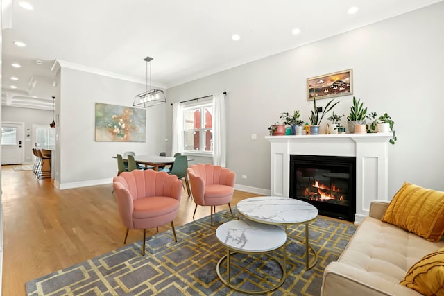 living room with recessed lighting, baseboards, light wood-style floors, ornamental molding, and a glass covered fireplace