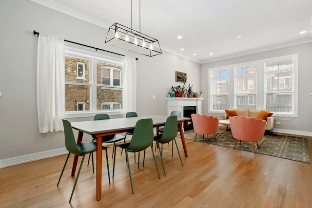 dining area featuring light wood finished floors, a lit fireplace, baseboards, and crown molding