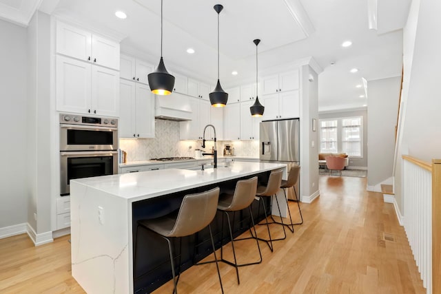 kitchen featuring appliances with stainless steel finishes, pendant lighting, white cabinets, and an island with sink