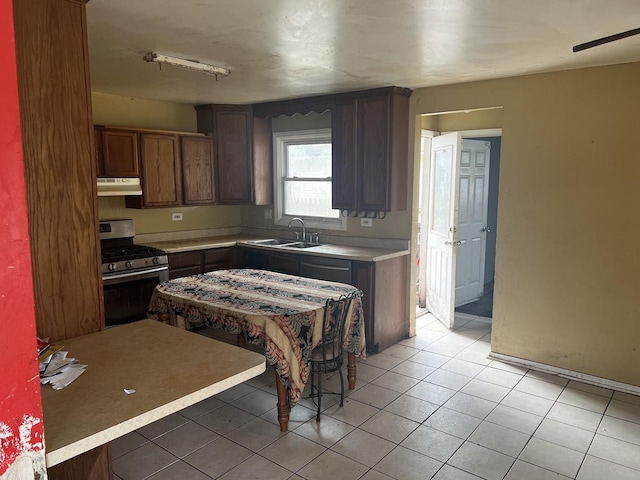 kitchen with light tile patterned floors, under cabinet range hood, a sink, light countertops, and gas range