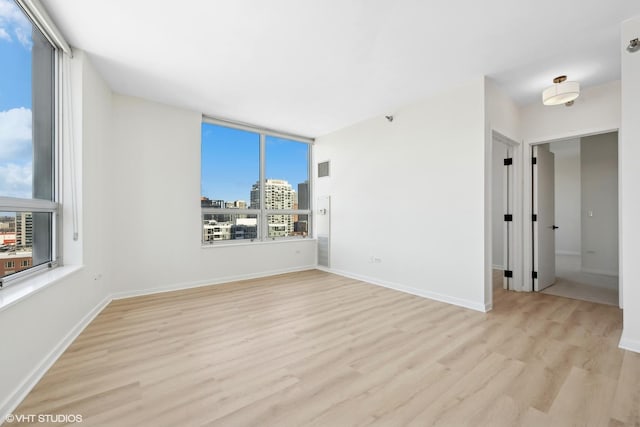 unfurnished room with a view of city, light wood-type flooring, visible vents, and baseboards