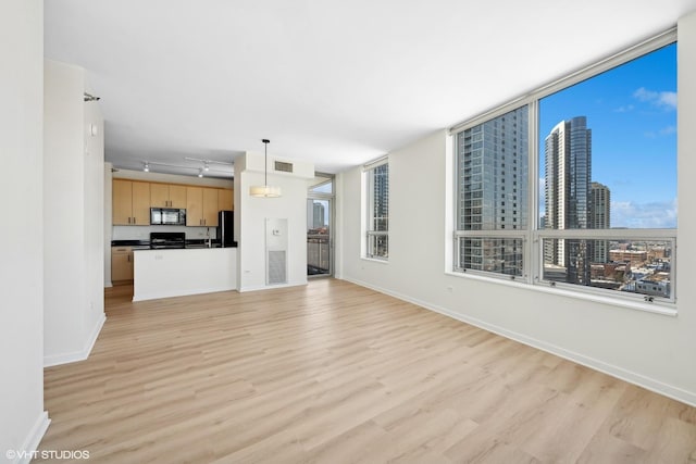 unfurnished living room with a view of city, visible vents, light wood-style flooring, and baseboards