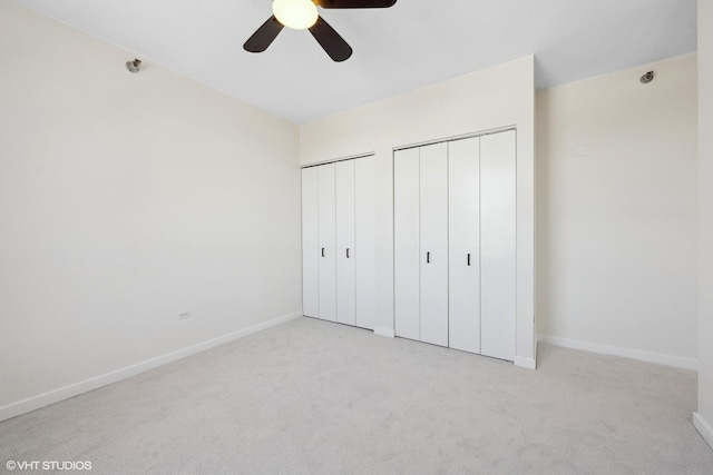 unfurnished bedroom with a ceiling fan, light colored carpet, baseboards, and two closets