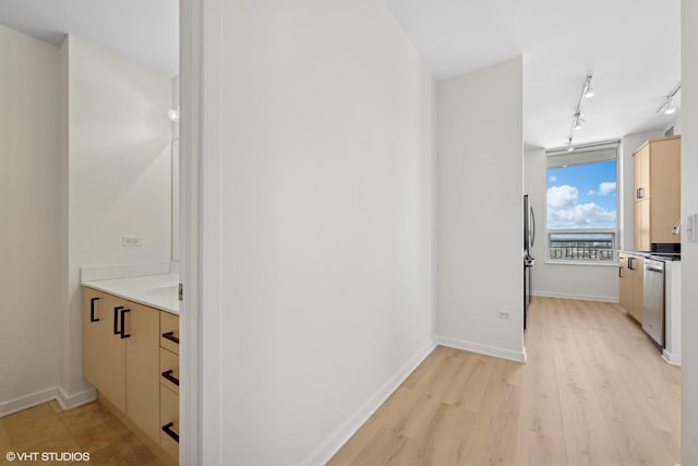 hall featuring light wood-style floors, baseboards, and rail lighting