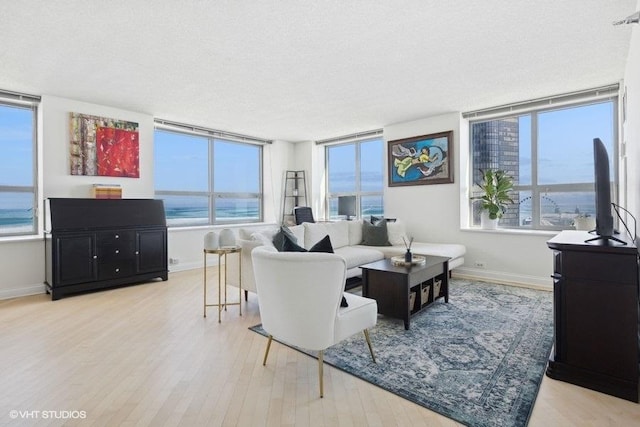 living room with a textured ceiling, a water view, light wood-style flooring, and baseboards