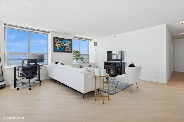 living area featuring light wood-type flooring, a lit fireplace, baseboards, and a textured ceiling