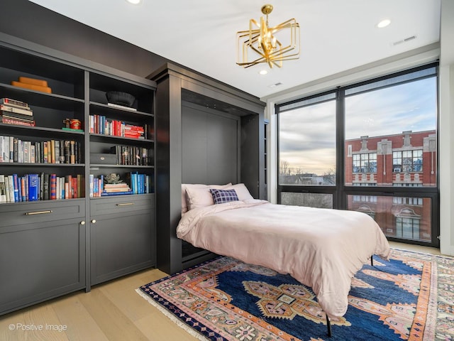 bedroom with a wall of windows, light hardwood / wood-style floors, and an inviting chandelier