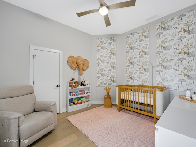 bedroom with a crib, ceiling fan, and light hardwood / wood-style floors