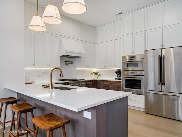 kitchen featuring a kitchen bar, custom range hood, decorative light fixtures, stainless steel appliances, and kitchen peninsula