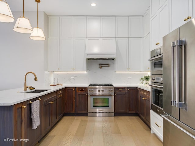 kitchen with premium appliances, sink, hanging light fixtures, and white cabinets