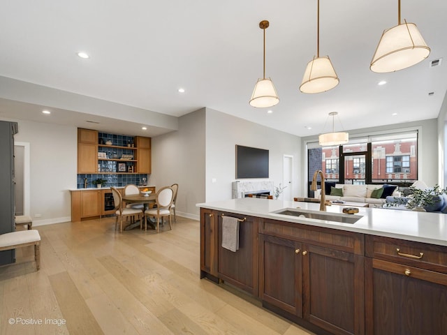 kitchen featuring pendant lighting, sink, backsplash, and light hardwood / wood-style flooring