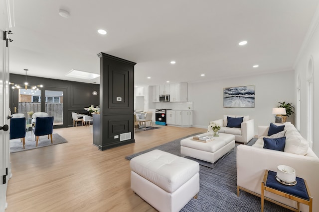 living room with a skylight, crown molding, a chandelier, and light hardwood / wood-style flooring