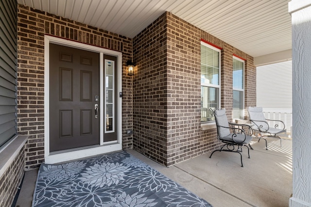 view of exterior entry featuring a porch and brick siding