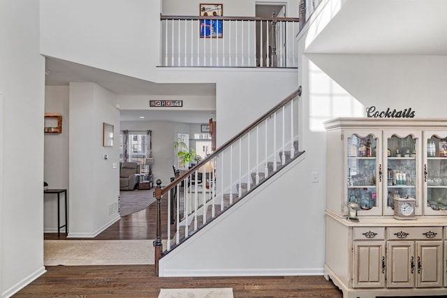 stairway featuring a towering ceiling, visible vents, baseboards, and wood finished floors