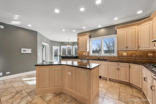 kitchen with decorative backsplash, a kitchen island, a sink, and light brown cabinetry