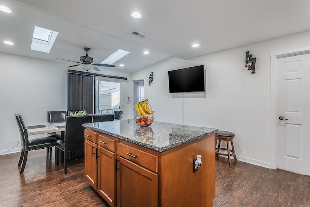 kitchen featuring brown cabinetry, dark wood-style flooring, dark stone countertops, a center island, and recessed lighting