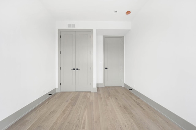 unfurnished bedroom featuring light wood-style floors, baseboards, visible vents, and a closet