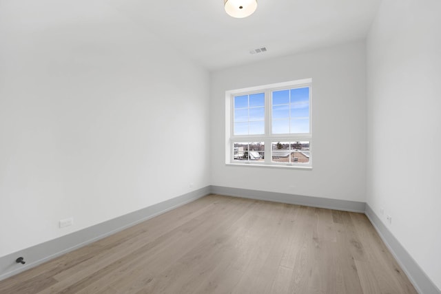 spare room with light wood finished floors, visible vents, and baseboards