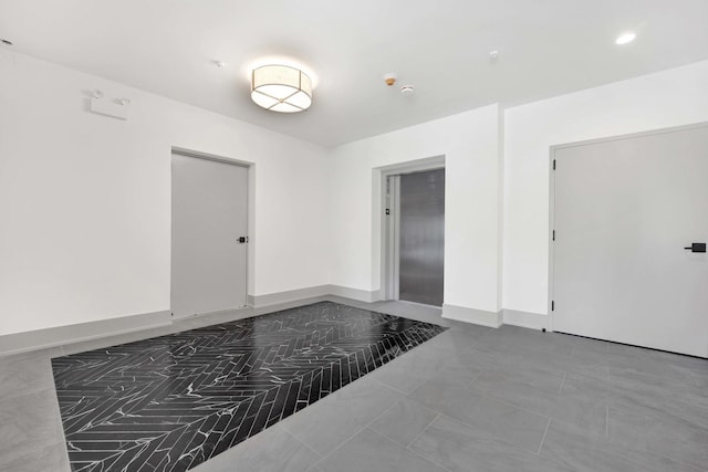 empty room featuring elevator and baseboards