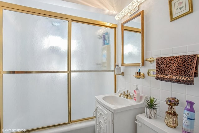 full bathroom with vanity, toilet, tile walls, and bath / shower combo with glass door