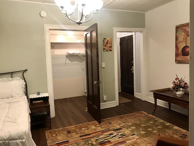 bedroom with an inviting chandelier, a walk in closet, a closet, dark hardwood / wood-style flooring, and ornamental molding