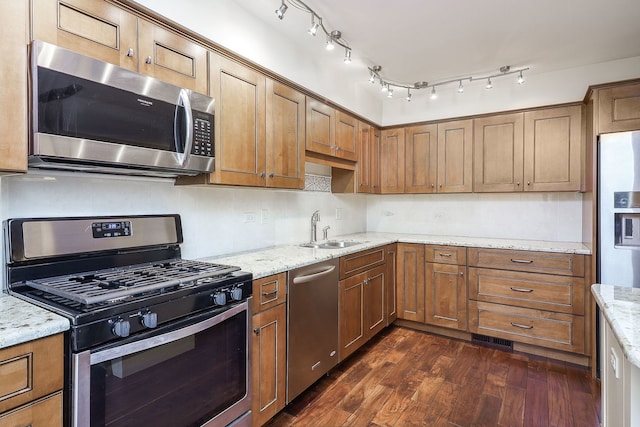 kitchen featuring dark wood-style flooring, appliances with stainless steel finishes, brown cabinetry, and a sink