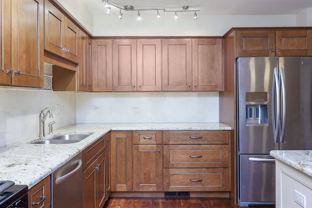 kitchen featuring brown cabinets, light stone countertops, stainless steel appliances, and a sink