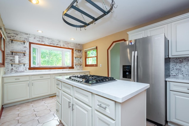 kitchen featuring tasteful backsplash, stainless steel appliances, white cabinets, light tile patterned flooring, and a center island