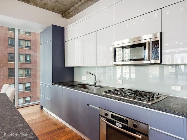 kitchen with light wood-type flooring, stainless steel appliances, decorative backsplash, sink, and white cabinetry