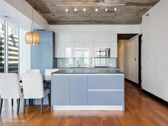 kitchen featuring hanging light fixtures, sink, backsplash, wood-type flooring, and white cabinets