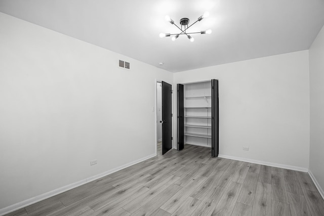 spare room featuring a chandelier and light hardwood / wood-style floors