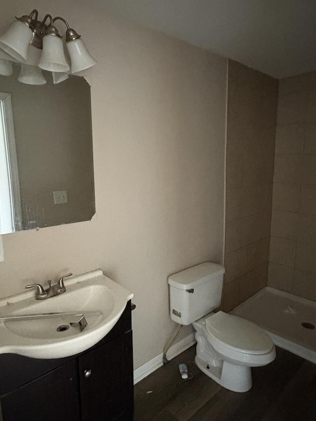 bathroom featuring toilet, wood-type flooring, vanity, and a tile shower