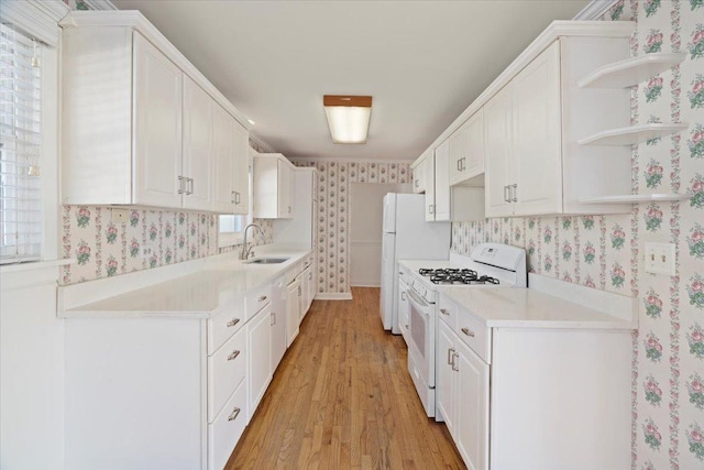 kitchen with wallpapered walls, white gas range, white cabinetry, open shelves, and a sink