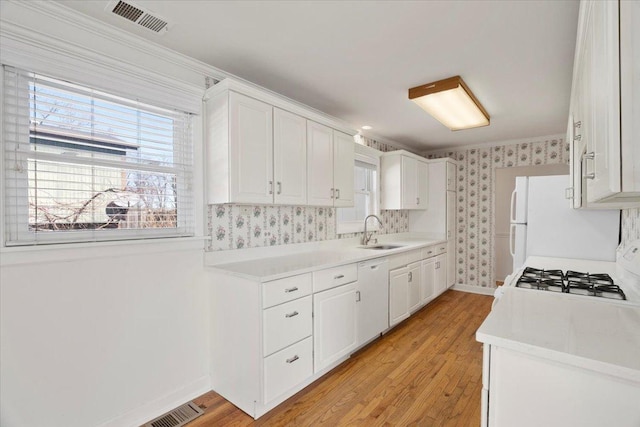 kitchen with light countertops, visible vents, white cabinets, a sink, and wallpapered walls