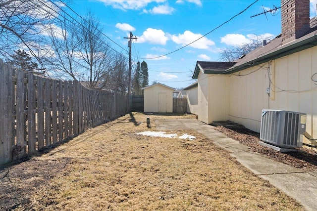 view of yard featuring an outbuilding, central air condition unit, a fenced backyard, and a storage unit