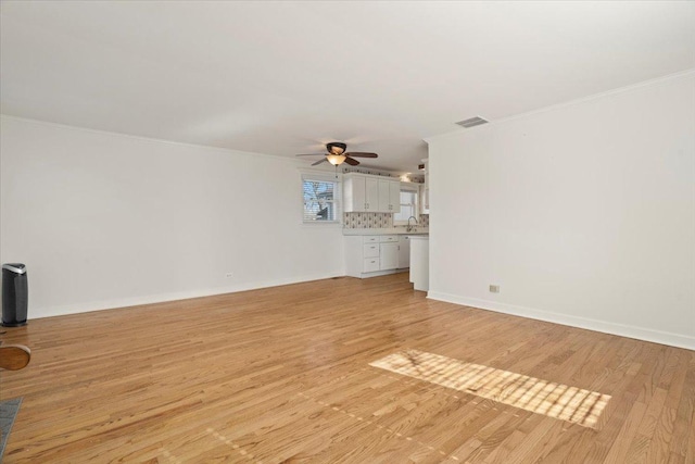 unfurnished living room featuring light wood finished floors, ornamental molding, a sink, and baseboards