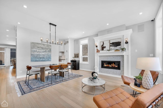 living area with light wood finished floors, baseboards, a glass covered fireplace, an inviting chandelier, and recessed lighting